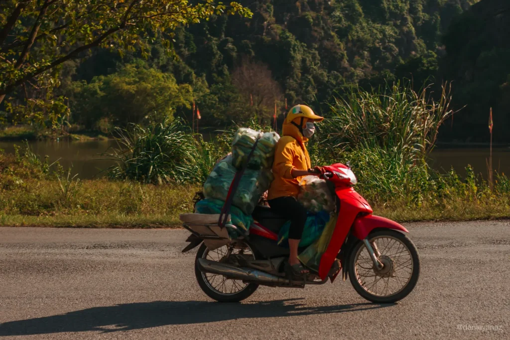Hombre manejando una motocicleta roja con bolsas llenas de frutas y verduras en Ninh Binh, Vietnam